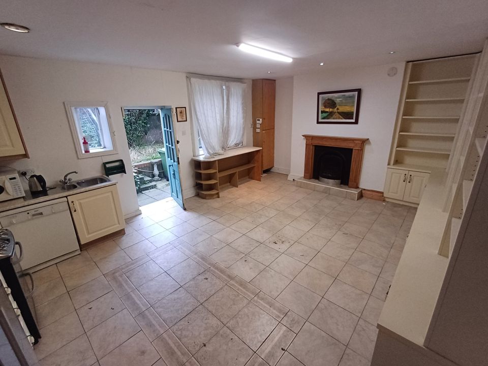 Empty open-plan kitchen and living area with tiled floor and bare shelving after clearance