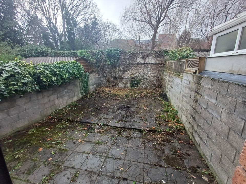 Cleared rear yard, bare paving between block walls after all junk and green waste removed