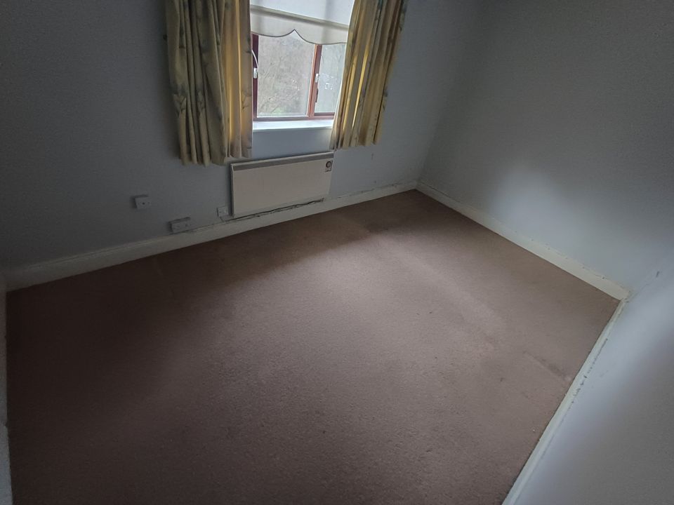 Empty carpeted bedroom with curtains left up after the furniture and contents were removed