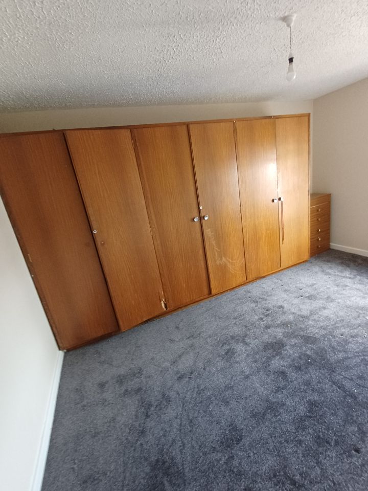 Cleared bedroom: grey carpet bare, only fitted wardrobes and small drawer unit left after clearance