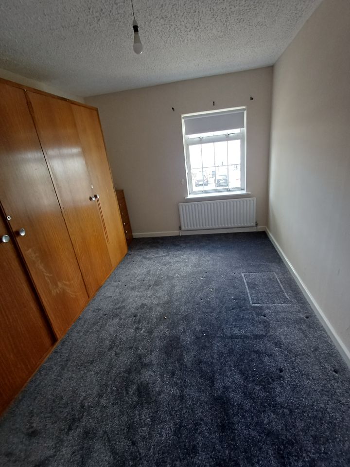 Empty bedroom with fitted wardrobes, window and radiator; carpet fully clear after house clearance