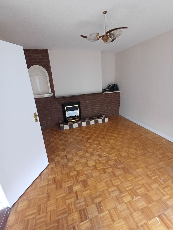 Empty living room with parquet floor, brick fireplace wall and ceiling light; fully cleared, bright
