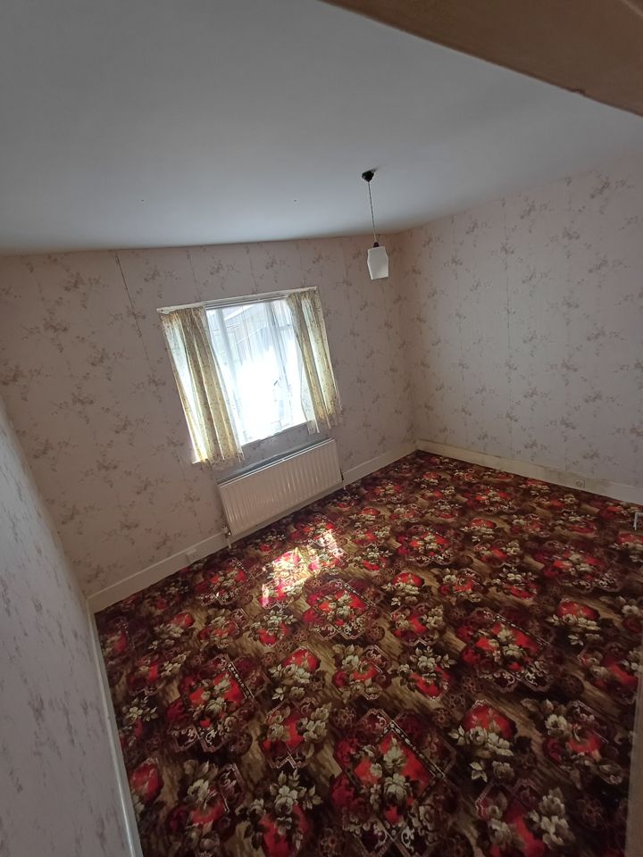 Bedroom emptied to bare walls and floral carpet, sunlight through window, ready for handover