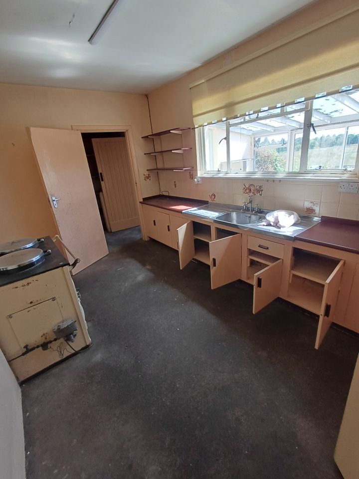 Old kitchen emptied: cupboard doors open and bare, range left in place, floor clear