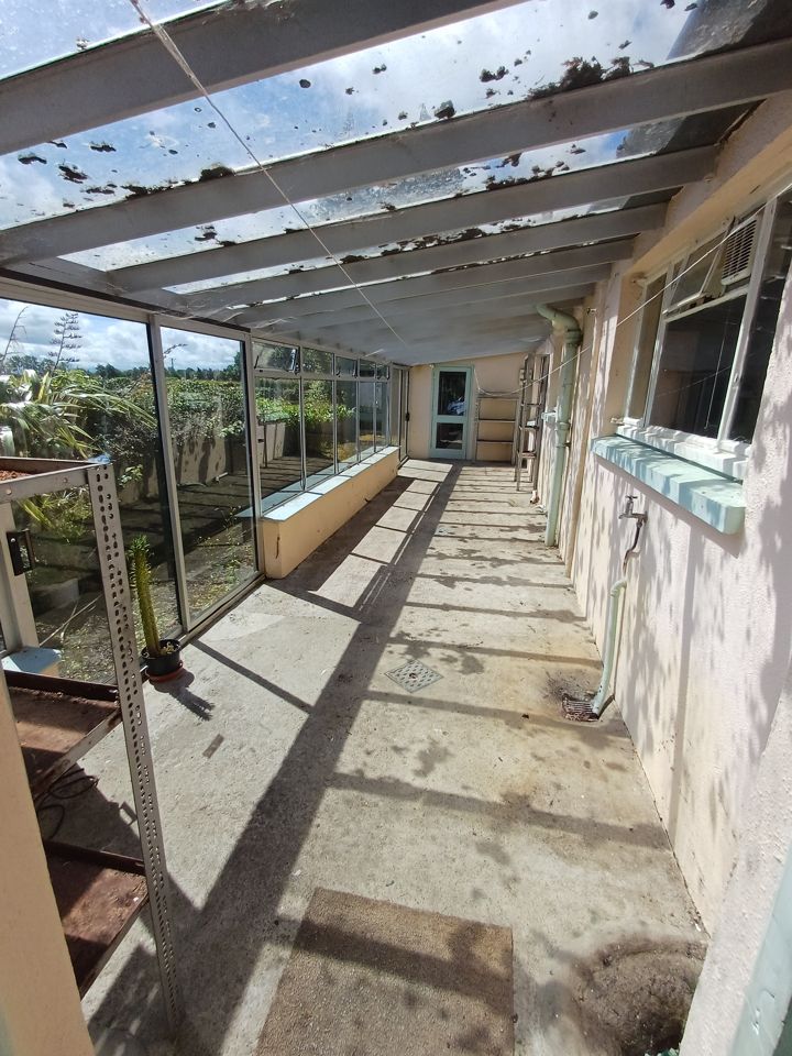 Glazed lean-to conservatory cleared down to bare concrete floor and empty metal shelving