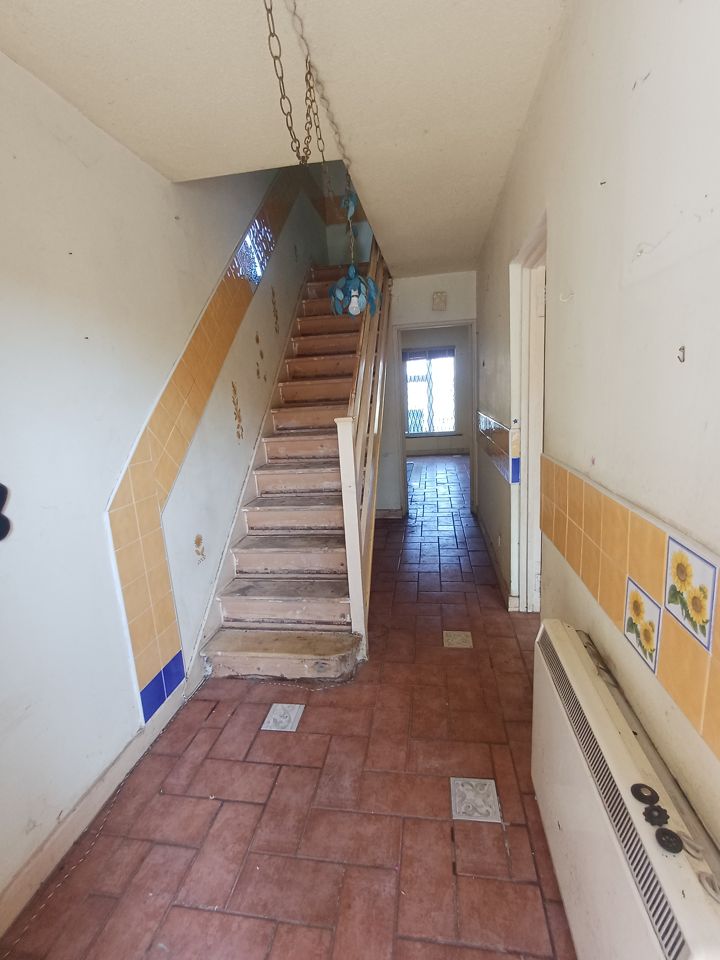 Cleared hallway and staircase of a house, bare tiled floor running to the back door
