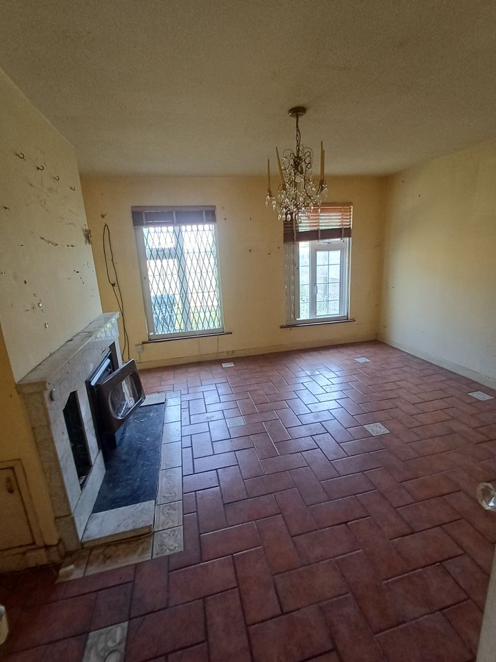 Fully emptied living room with marble fireplace, chandelier and herringbone tiled floor, bright and clean