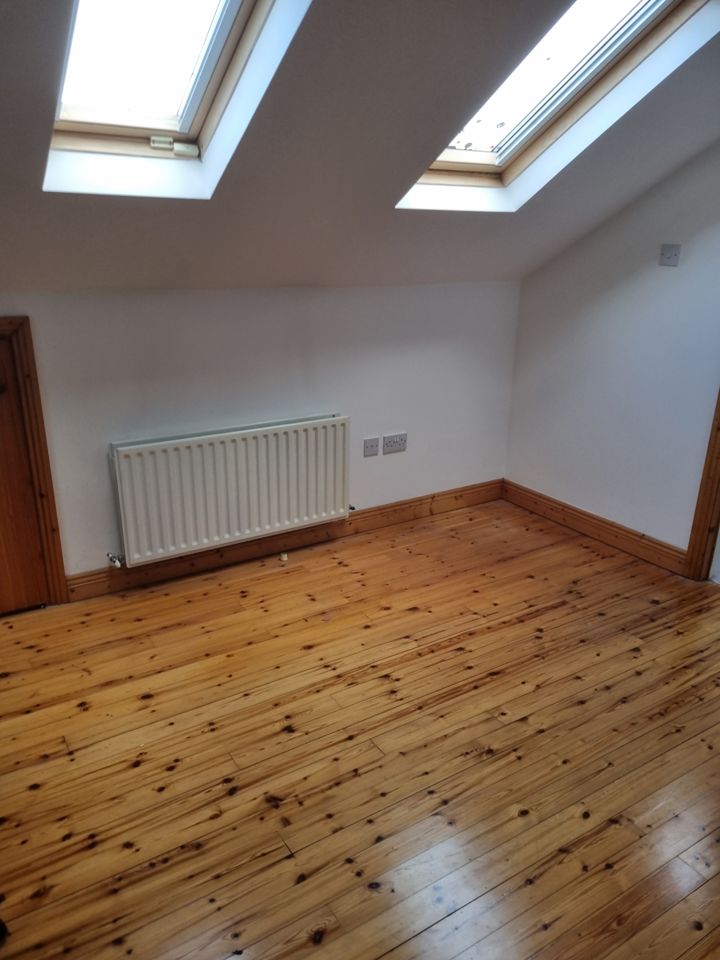 Emptied loft room with Velux windows, radiator and bare polished pine floor after clearance