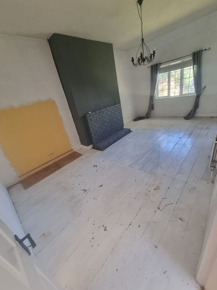 Fully emptied living room with bare painted floorboards, fireplace, chandelier and curtained window