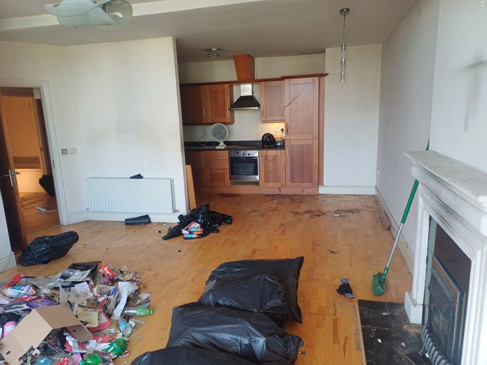 Open-plan apartment living room and kitchen mid-clearance, litter and bin bags across the floor