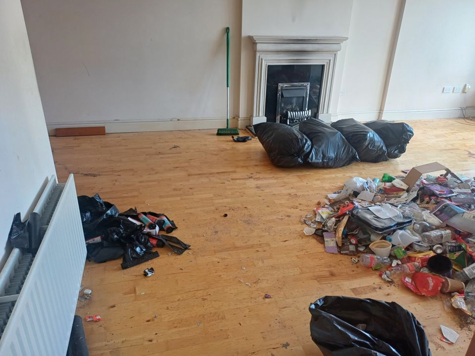 Apartment living area by fireplace, rubbish pile and black bags on wooden floor awaiting removal