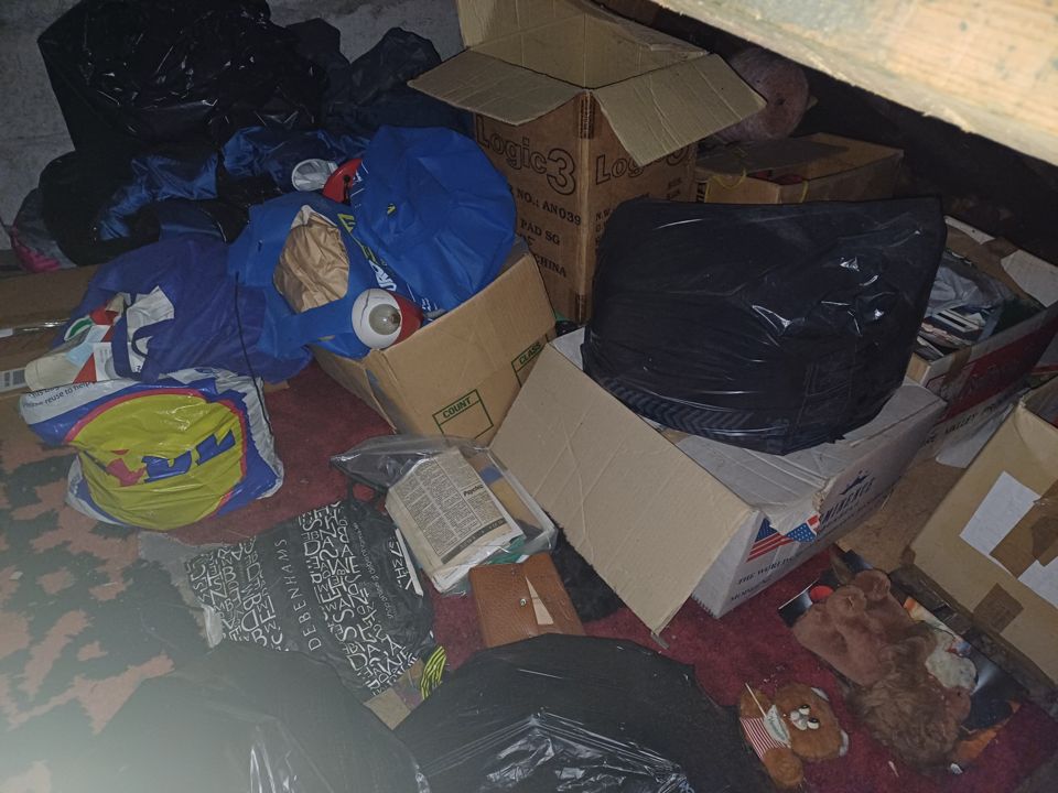 Attic floor crowded with open cardboard boxes, shopping bags and black sacks before a clearance
