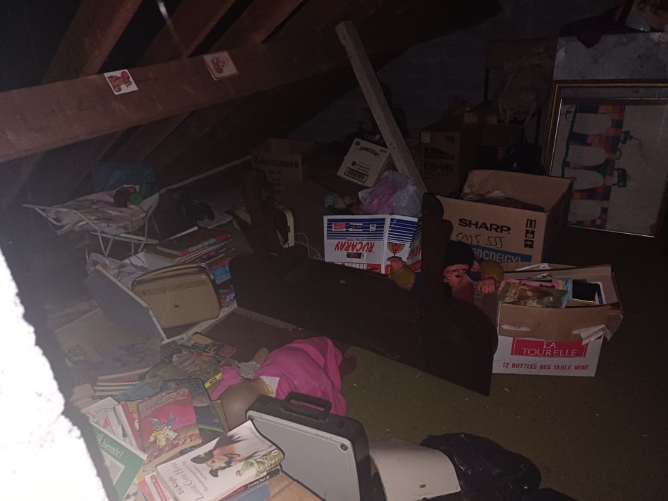Packed attic under the rafters with boxes, books, picture frames and bags spread across the floor