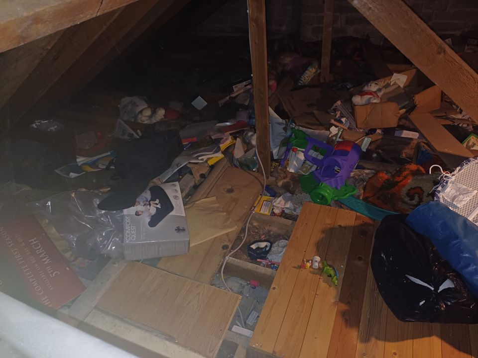 Heavily cluttered attic, boards and insulation buried under toys, boxes, bags and loose debris