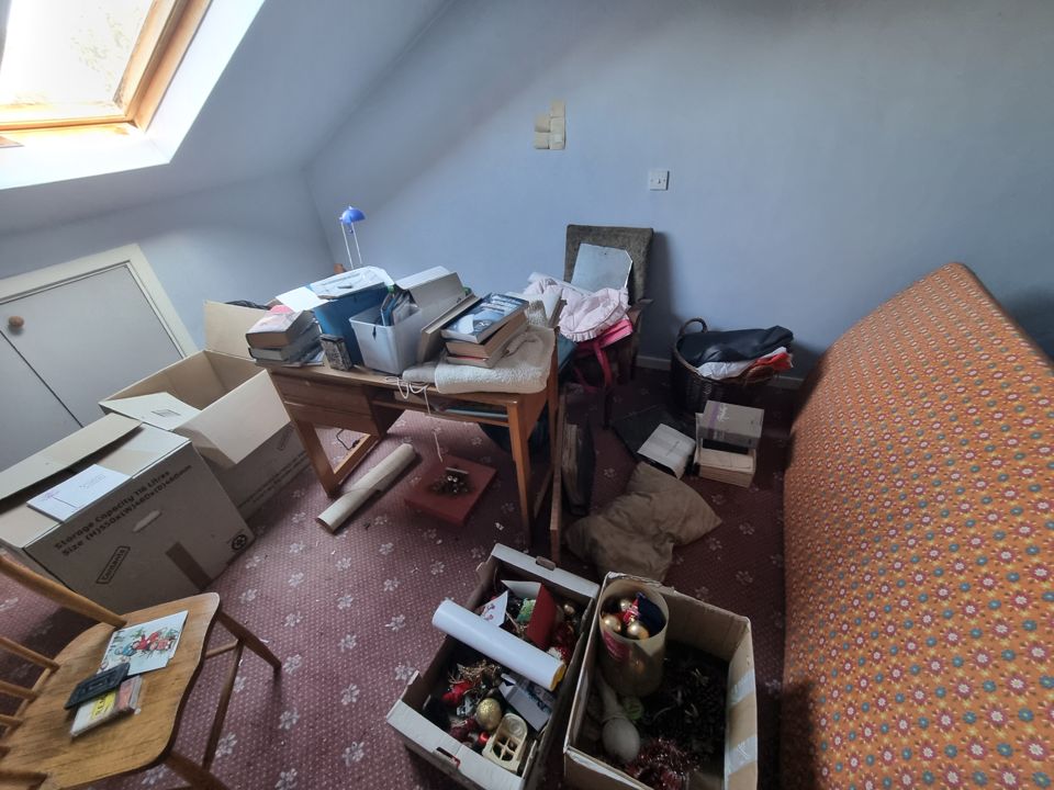 Converted attic bedroom under a Velux, boxes, desk clutter and mattress awaiting clearance
