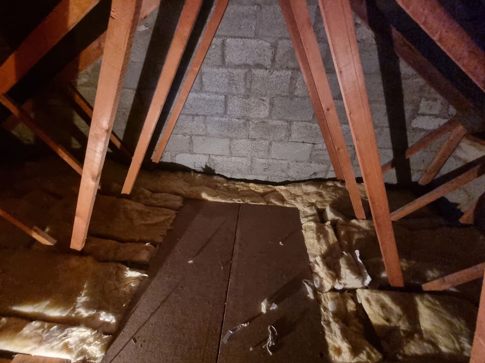Emptied boarded attic with roof trusses, block gable wall and insulation after clearance