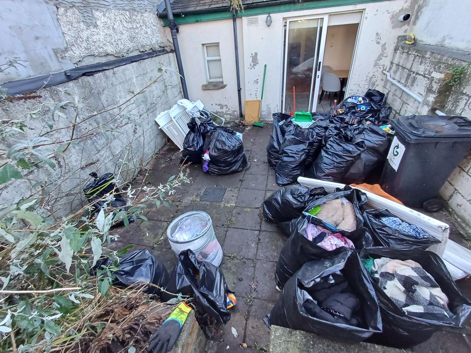 Small back yard filled with black rubbish bags, a wheelie bin and household junk awaiting removal