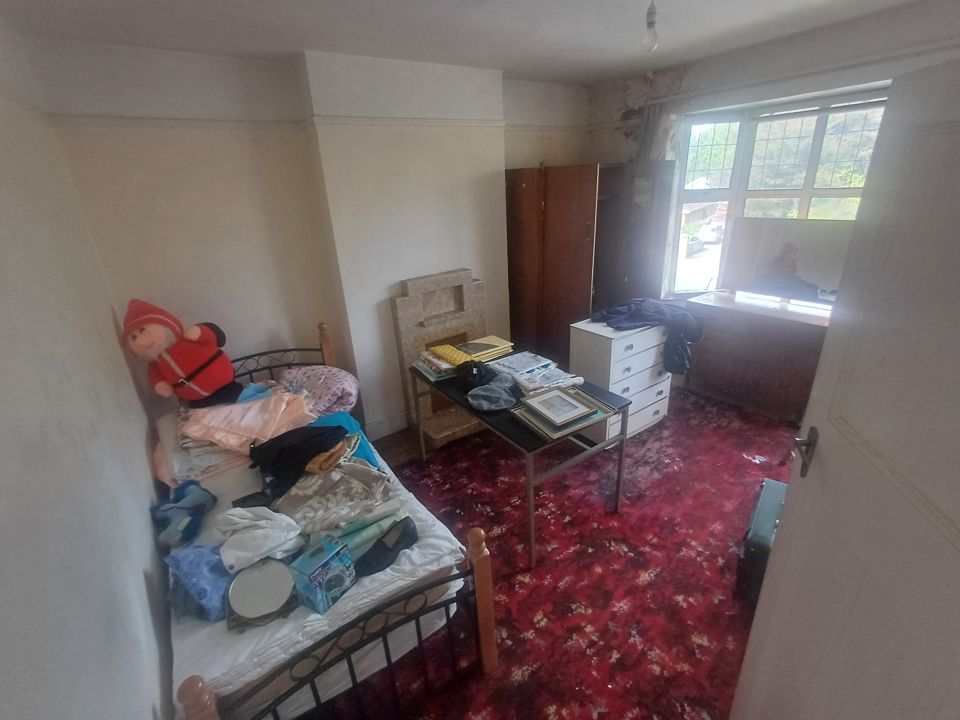 Bedroom in an older house with bed, drawers and wardrobe covered in belongings before clearance