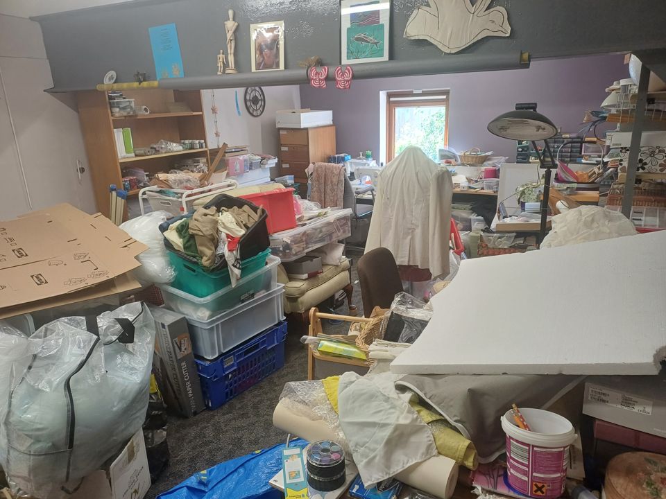 Craft room crammed with boxes, crates, bags, fabric and furniture; floor almost completely buried