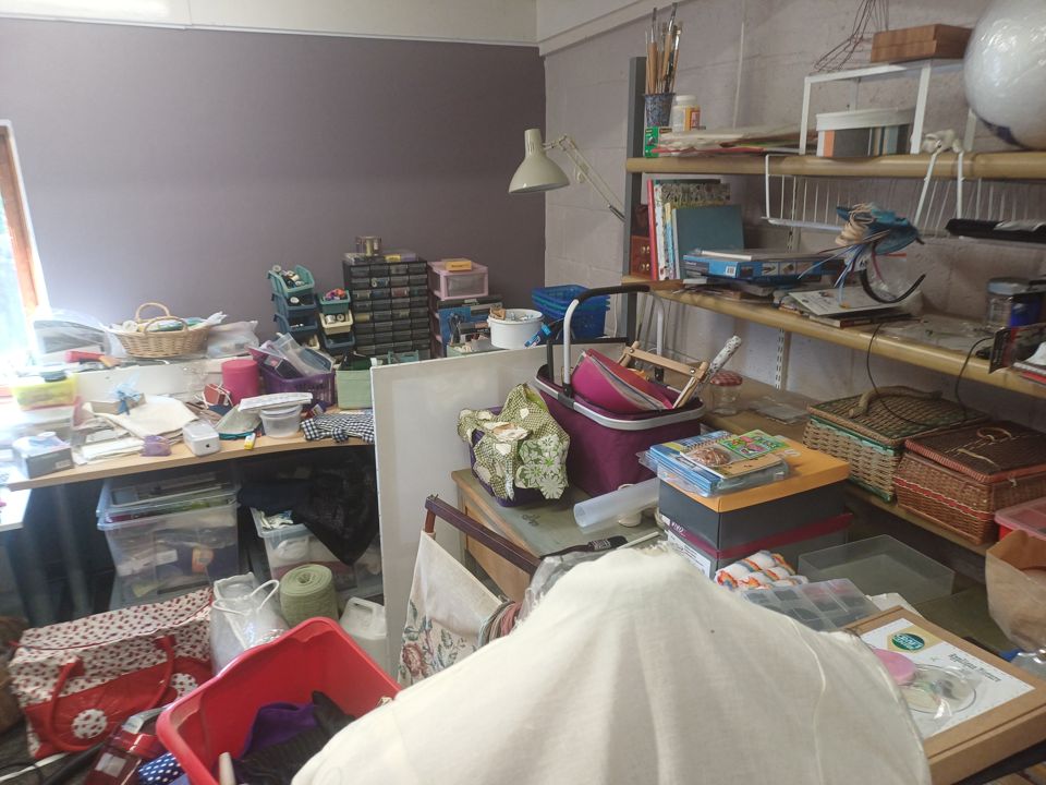 Overloaded shelving and desks with craft supplies, baskets and bags filling a spare room
