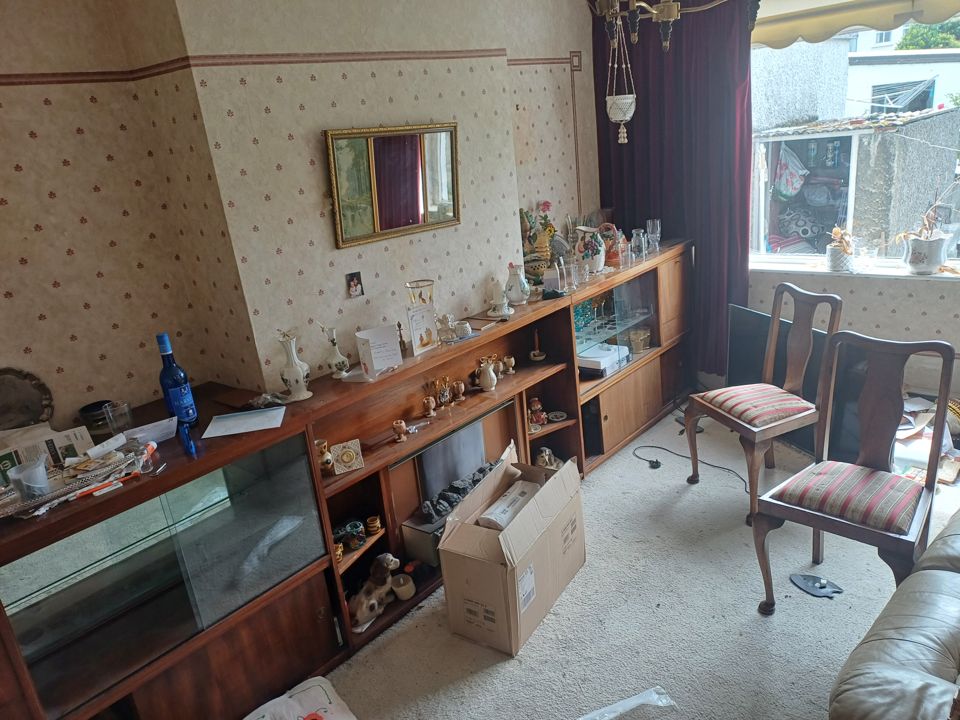 Dated living room with display cabinets full of ornaments, chairs and boxes before house clearance