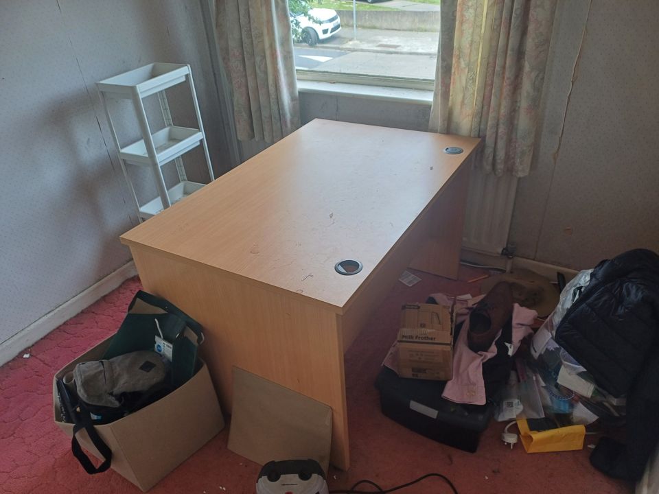 Bedroom with desk, bags and boxes scattered on the floor awaiting removal