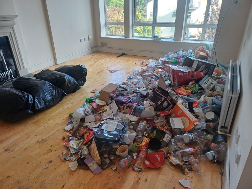 Apartment living room with a large heap of hoarded rubbish and full black bin bags