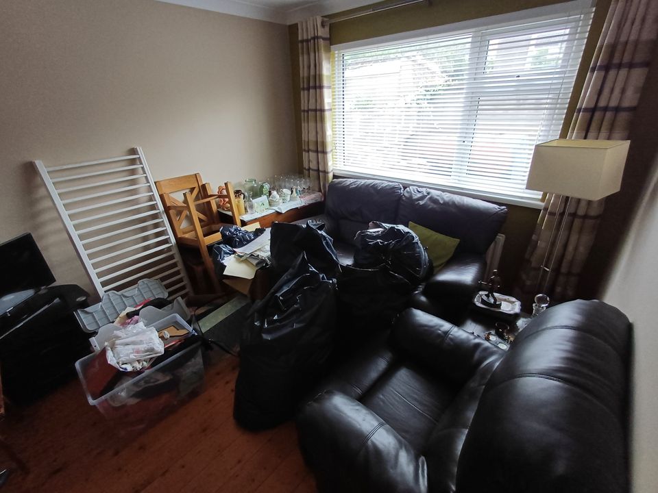 Living room with leather sofas, bin bags, cot side, storage boxes and glassware gathered for clearance