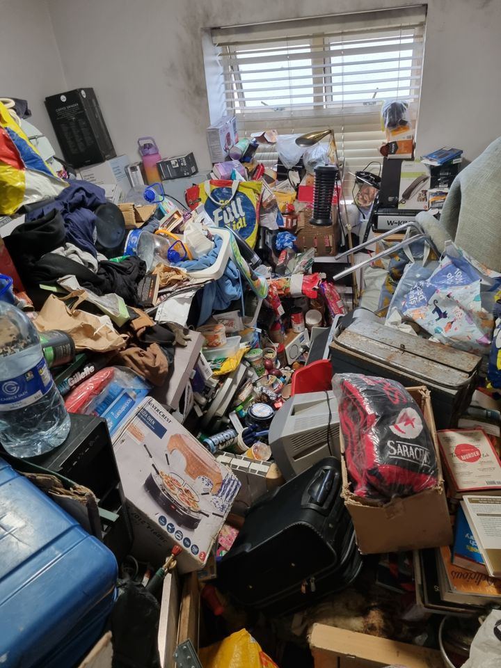 Hoarded bedroom with floor completely buried under bags, boxes, clothes and household junk