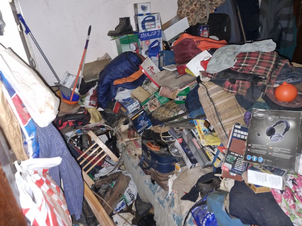 Bedroom in a hoarded house, bed and floor buried under clothes, boxes and tools
