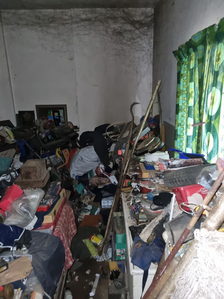 Damp hoarded room piled with junk, tools and bags right up to the window