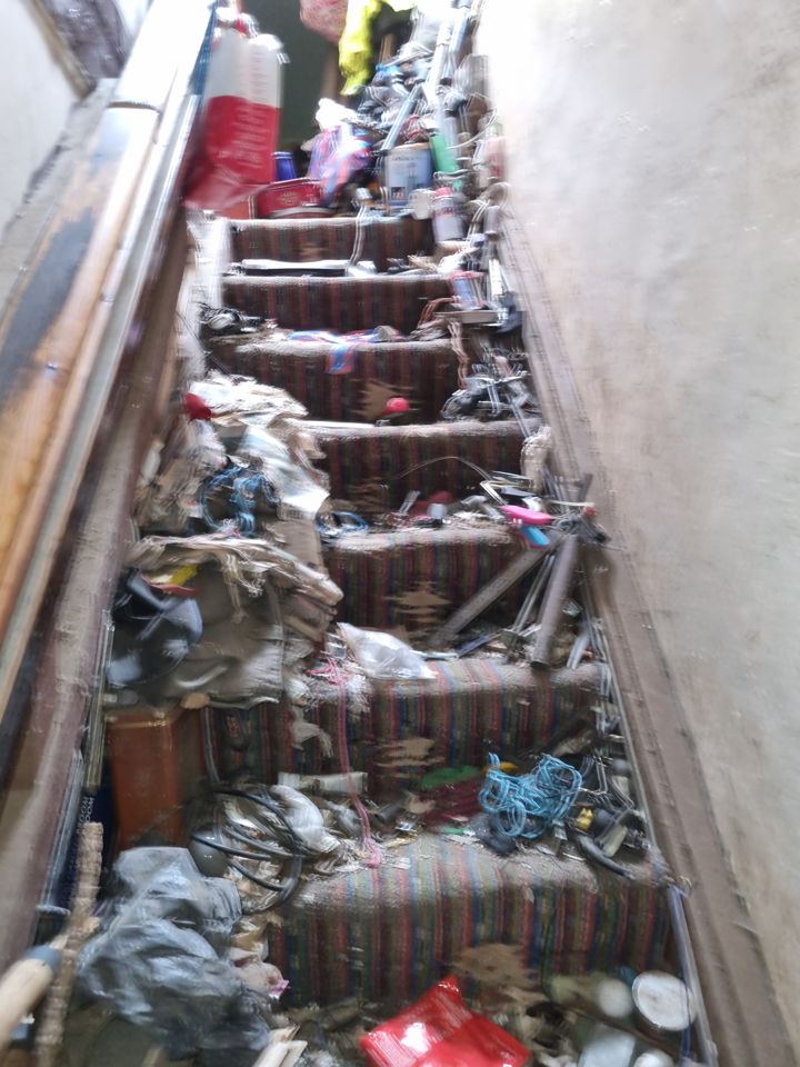 Narrow staircase in a hoarded house with every step covered in rubbish and clutter
