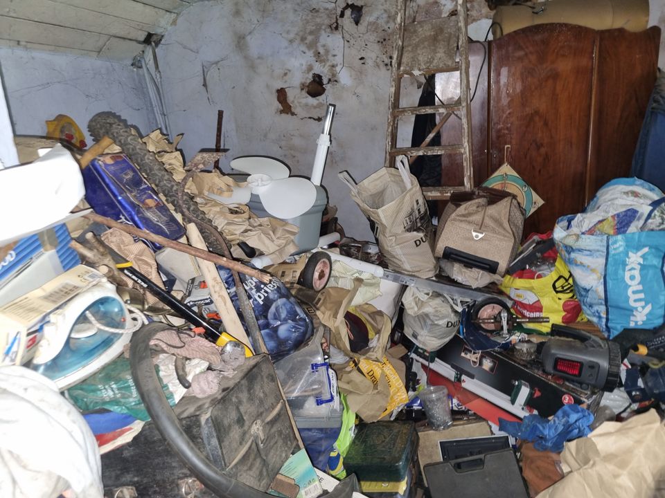 Hoarded room with bicycle, ladder, wardrobe and heaped bags covering the entire floor