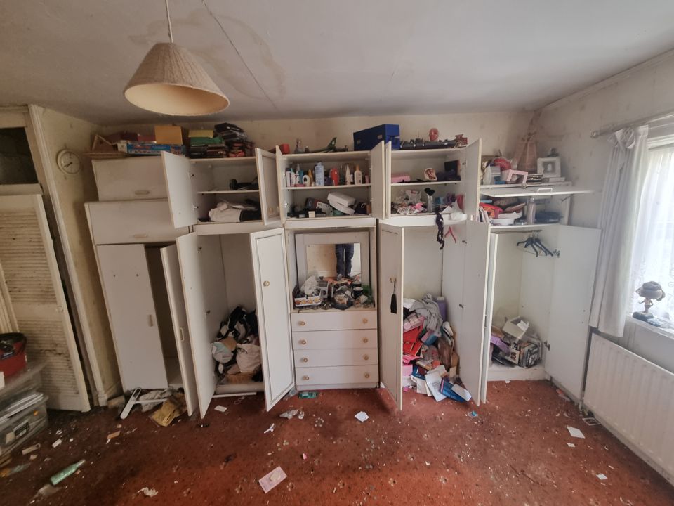 Bedroom fitted wardrobes flung open, contents spilling onto a littered, stained carpet