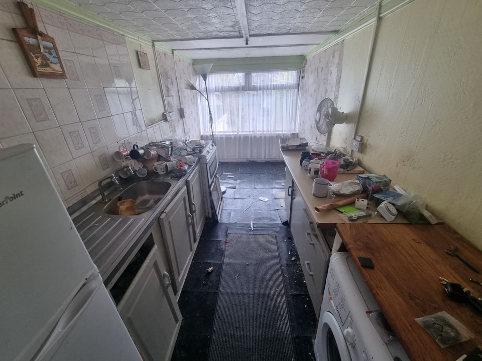 Galley kitchen cluttered with mugs, boxes and rubbish, debris across the floor tiles