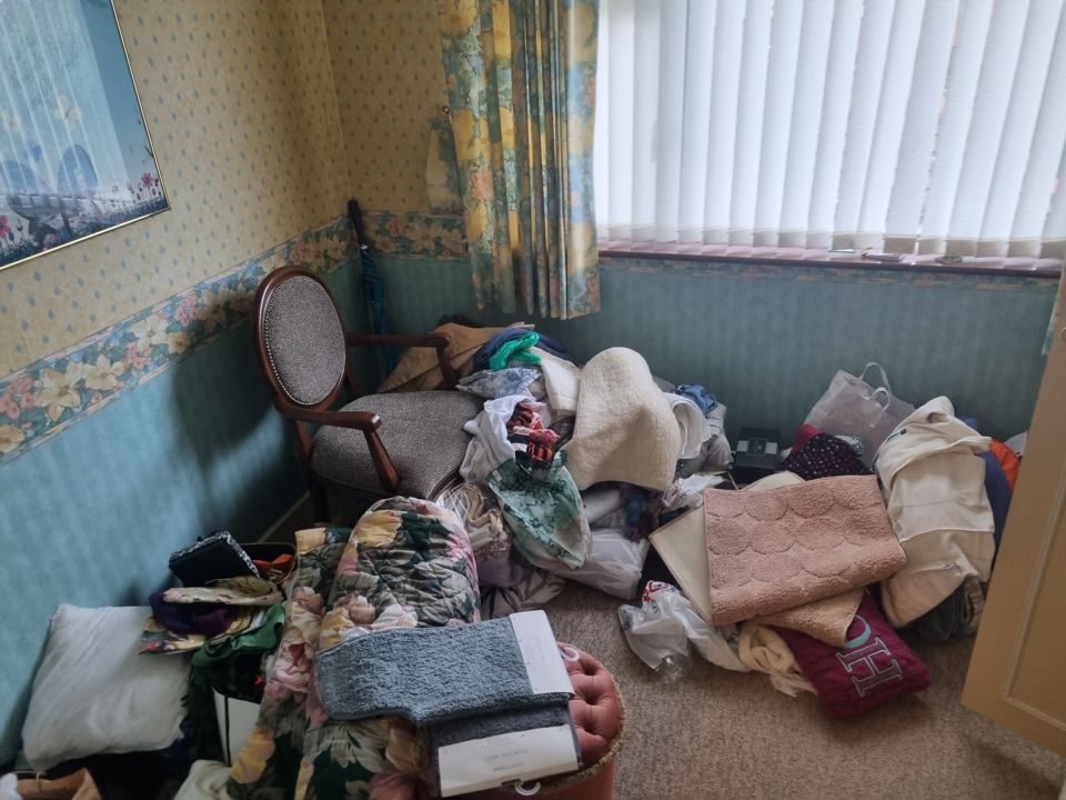 Small bedroom floor piled with clothes, bedding, mats and bags ready to clear