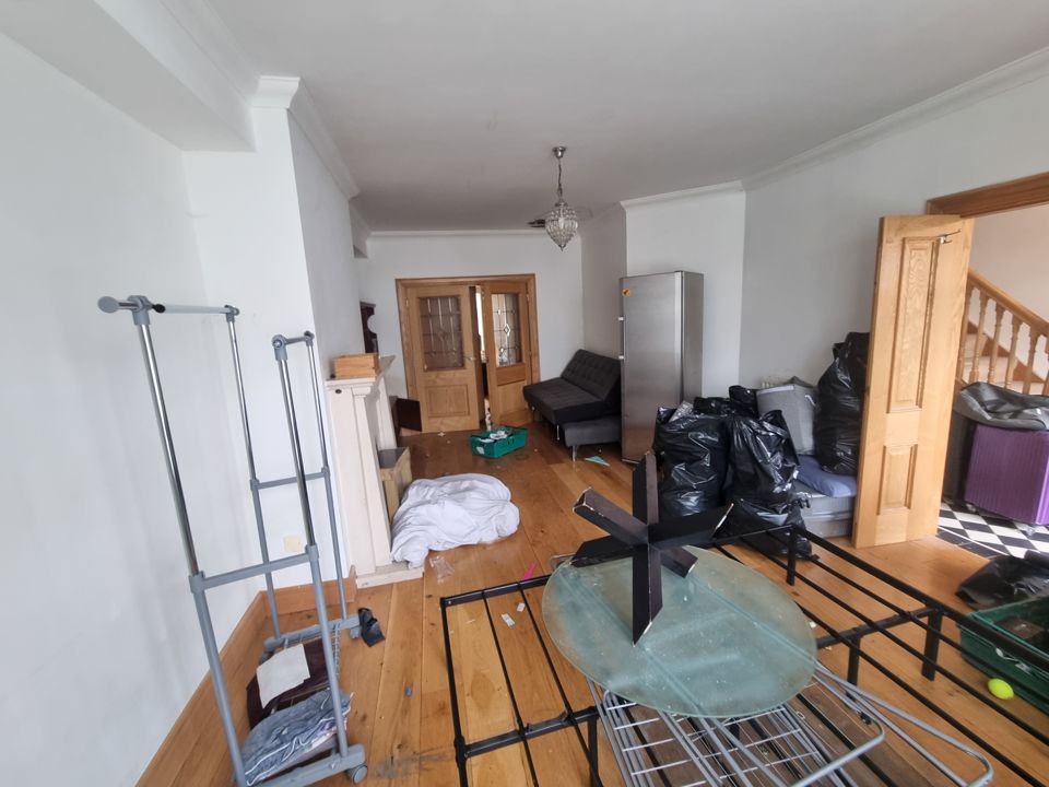 Through-lounge mid-clearance with bin bags, dismantled bed frame, clothes rails and glass table