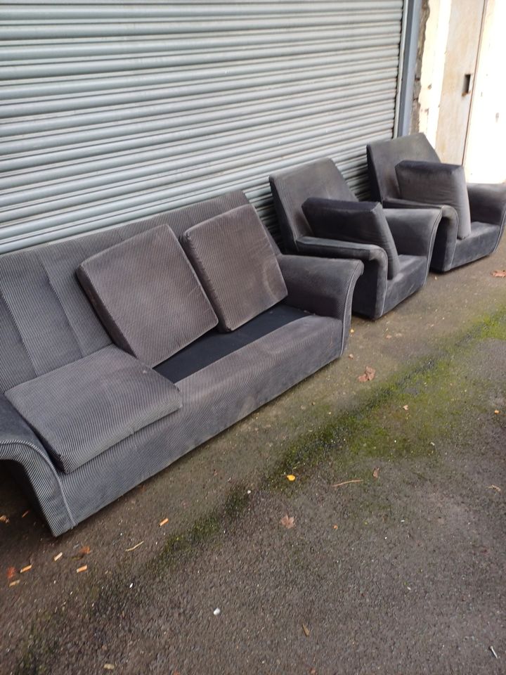 Old grey three-piece suite lined up outside a roller shutter, collected for removal and disposal