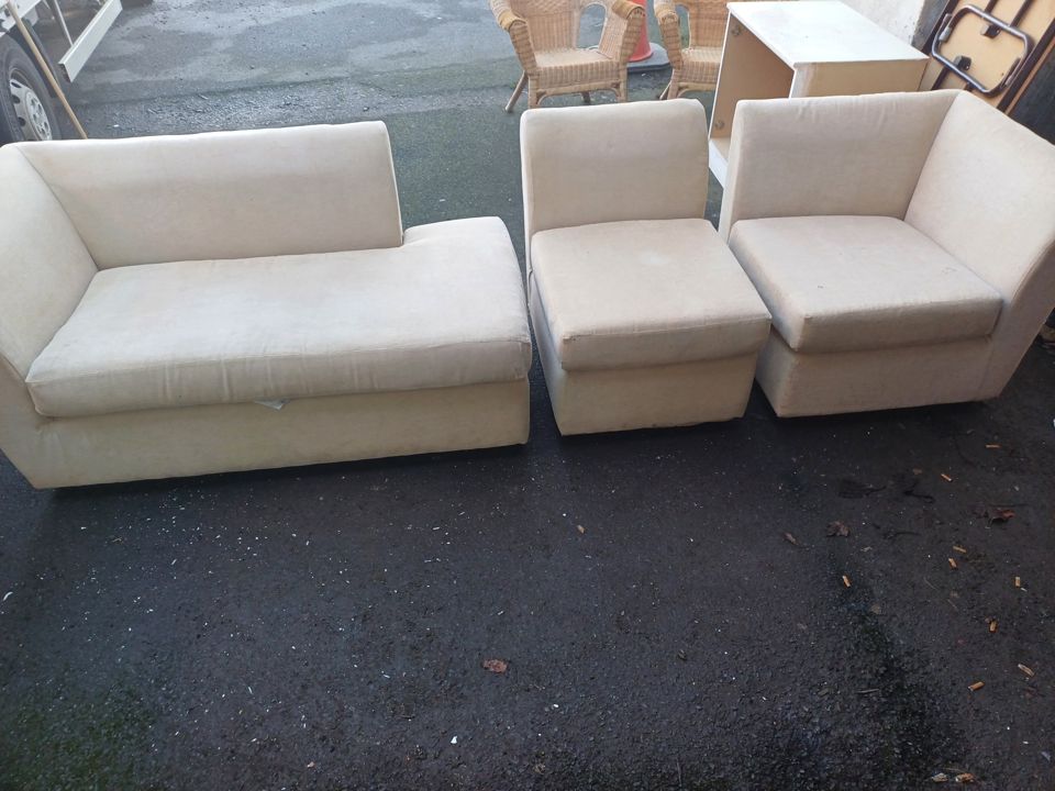 Cream sectional sofa pieces, wicker chairs and cabinet unloaded in a yard after a house clearance