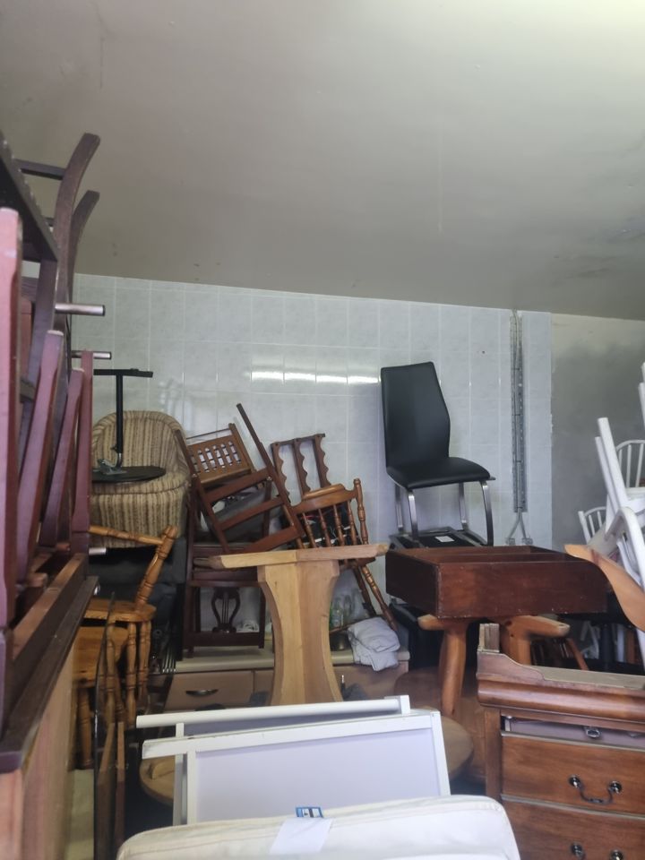 Chairs, tables, chests and drawers stacked tightly in a tiled room awaiting removal