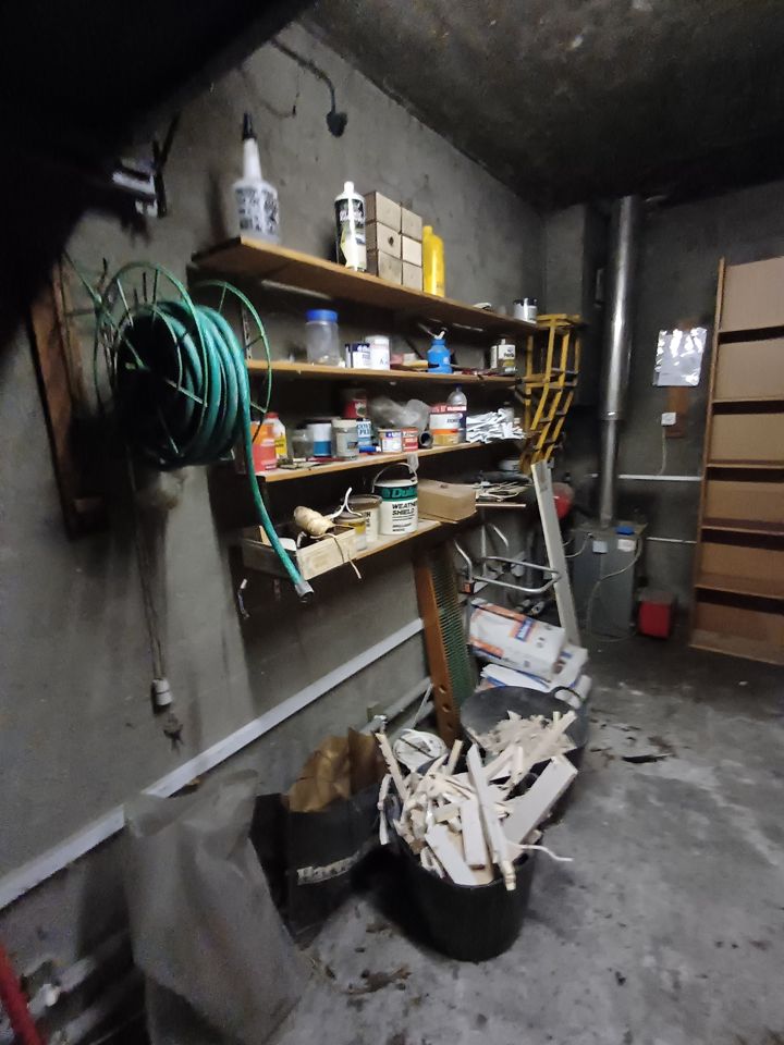 Garage shelves crammed with paint tins, hose reel, bins of offcuts and plaster bags before clearance
