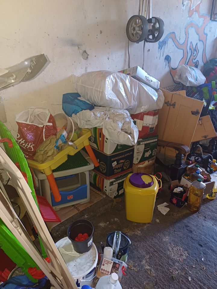 Garage corner stacked with sacks, cardboard boxes, a child's table and household clutter