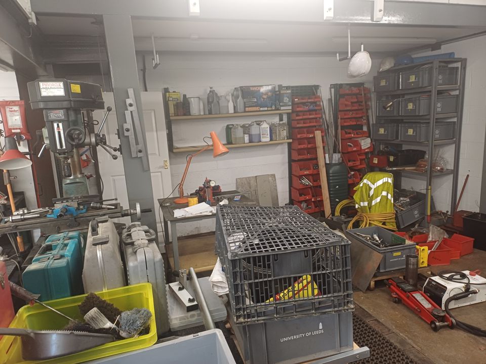 Garage workshop with pillar drill, crates, cages and tool racks crowding the floor