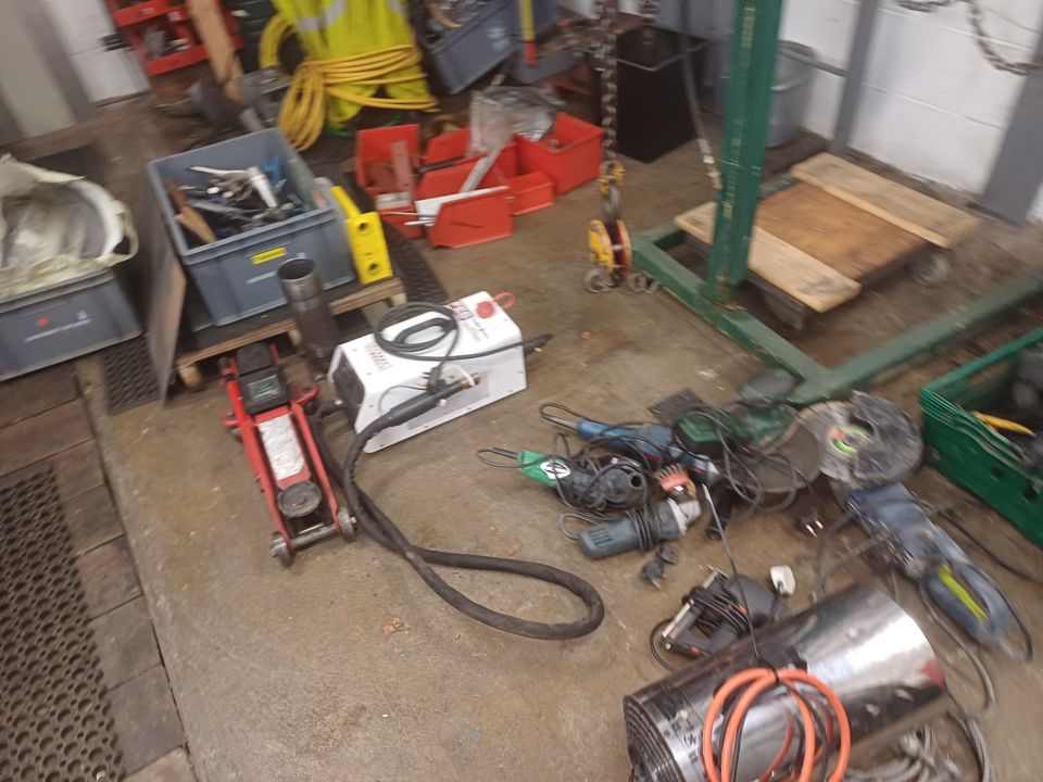 Garage floor strewn with power tools, trolley jack, crates and cables before clearance