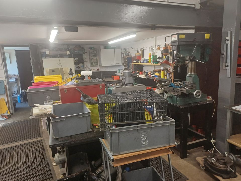 Long workshop garage lined with benches, machinery, crates and shelving full of stock