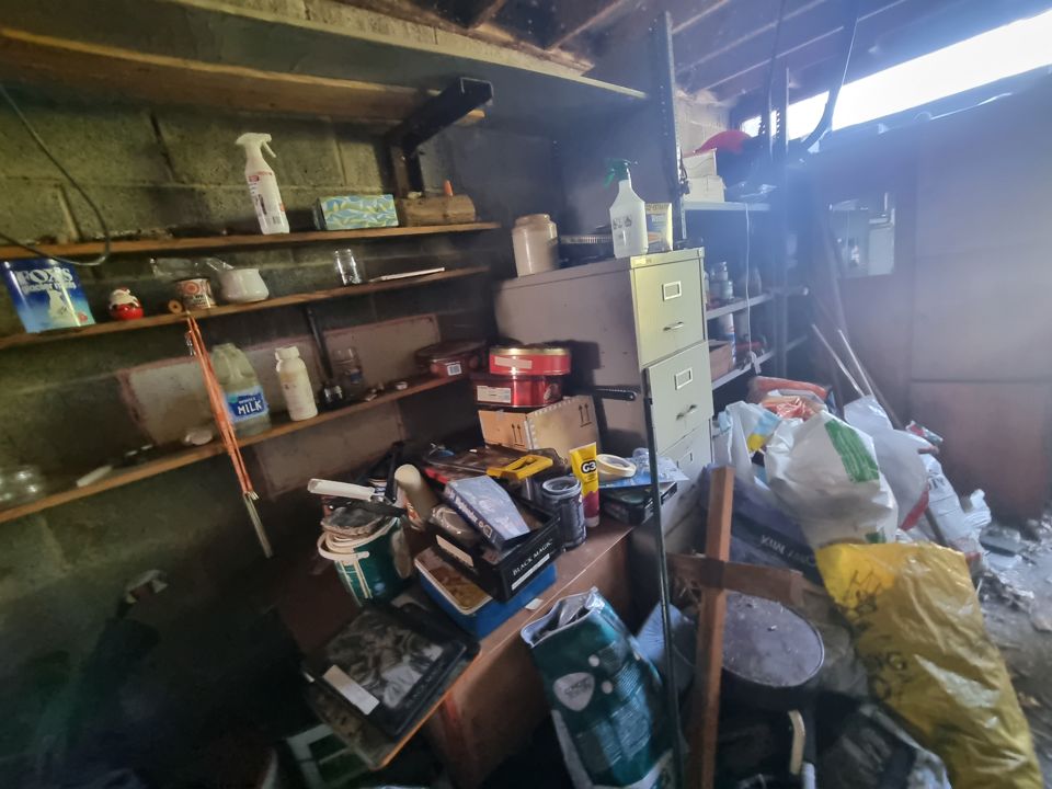 Garage shelving and filing cabinet loaded with paint, tins, bags and old household junk