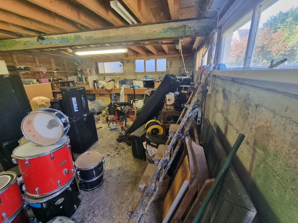 Large garage workshop with drum kit, speakers, timber and junk spread across the floor