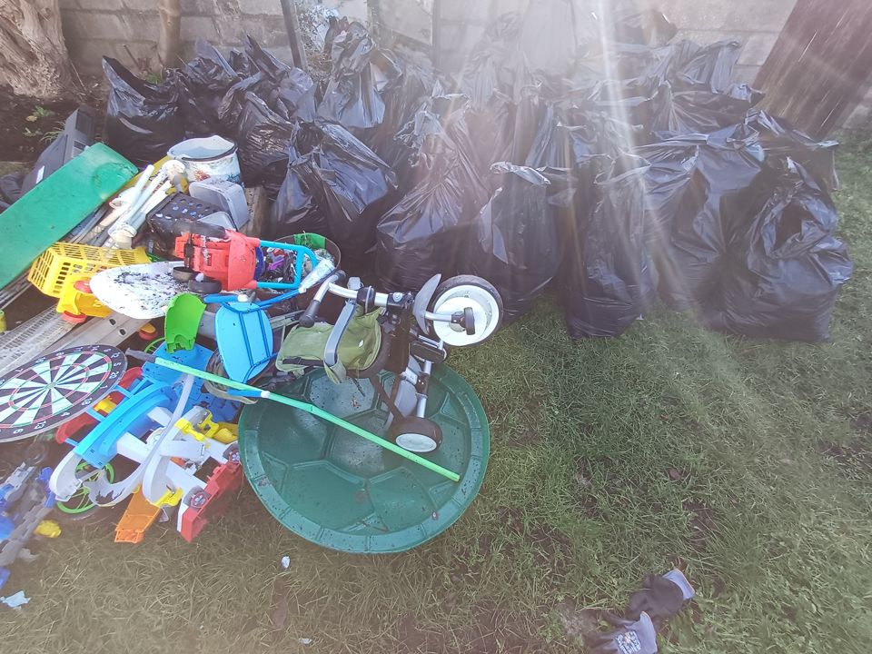 Wall of black bags plus broken toys and a dartboard piled on a lawn for collection