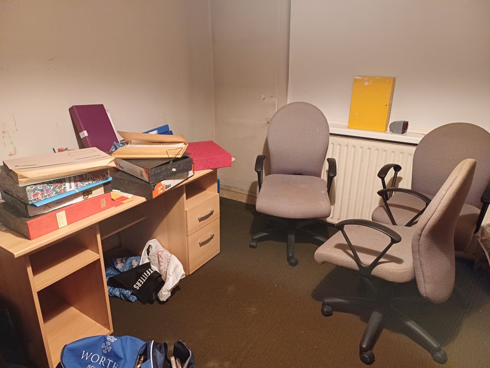 Home office before clearance: desk stacked with box files, three worn office chairs; crop bottom bag logo