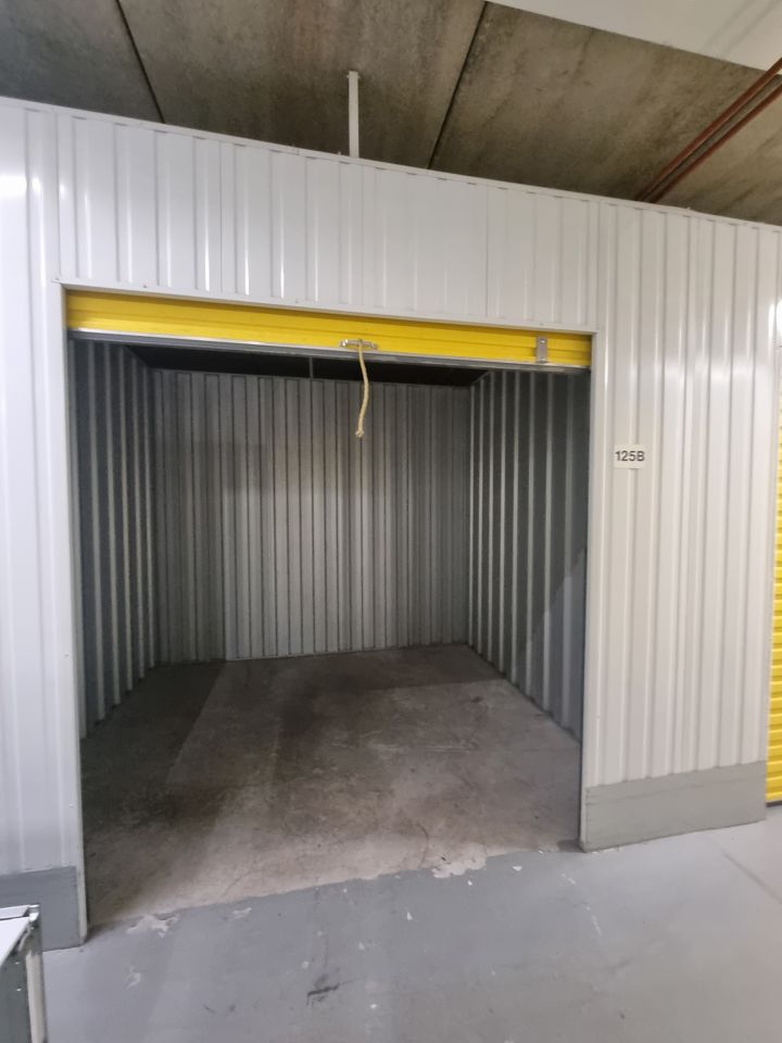 Cleared storage unit with yellow roller door open, bare corrugated walls and concrete floor
